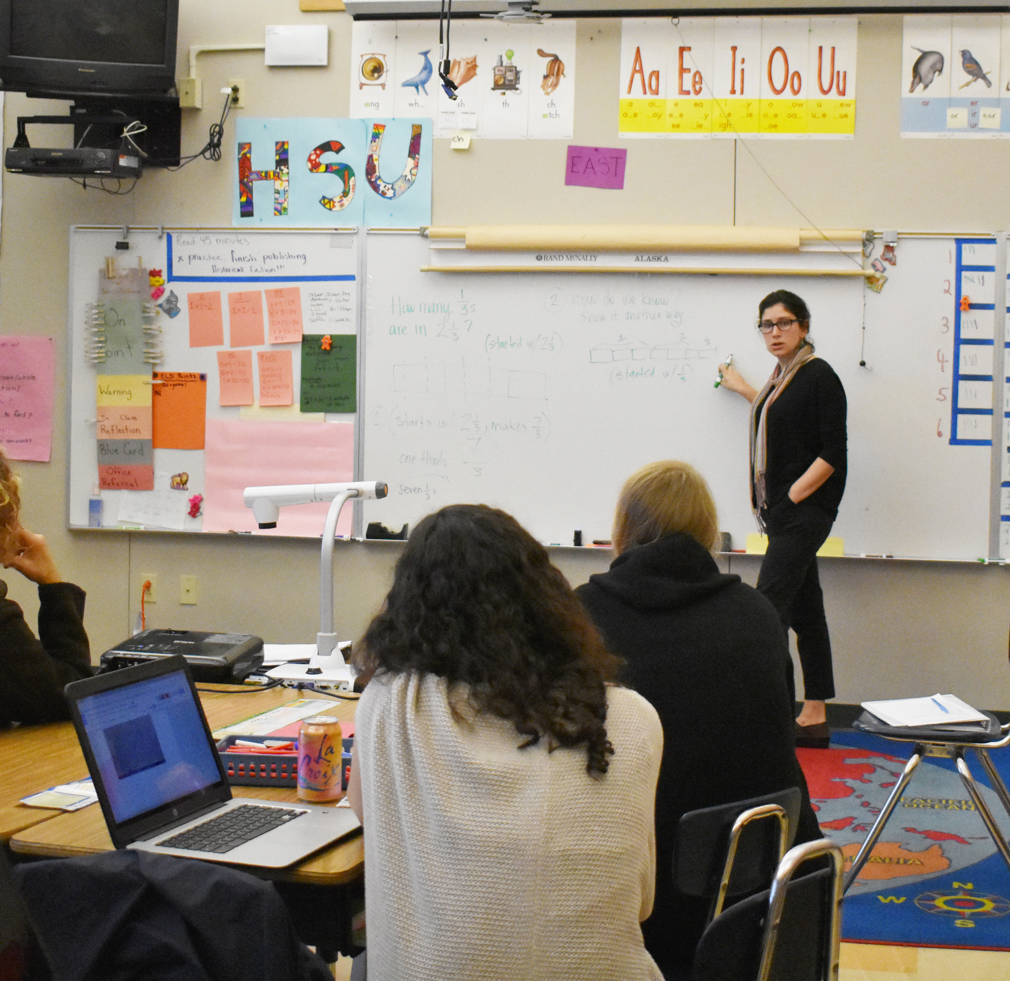 Teachers doing lesson planning look on as another teacher discusses equations written on a white board