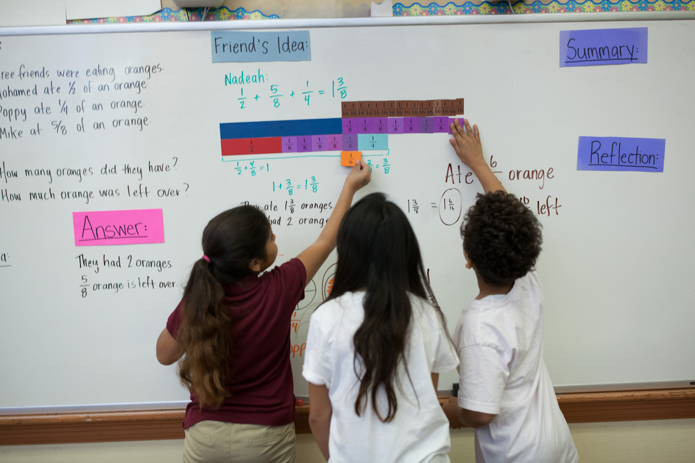 An elementary-age male student points while his female teacher stands beside him and observes